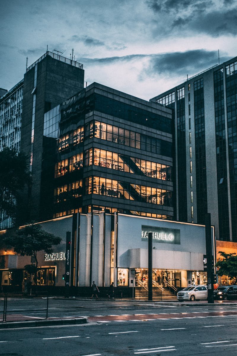 Night view of a city block with illuminated store, modern architecture, and cloudy sky.